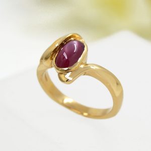Oval ruby cabochon gemstone in 18k yellow gold ring with accent diamonds and satin finish, designed by Morgan's Treasure in Westerville, OH