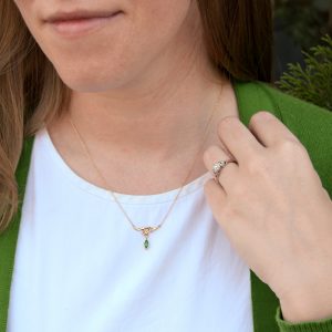Model wearing custom necklace in 14k yellow gold with branch design and marquise cut natural emerald dangle