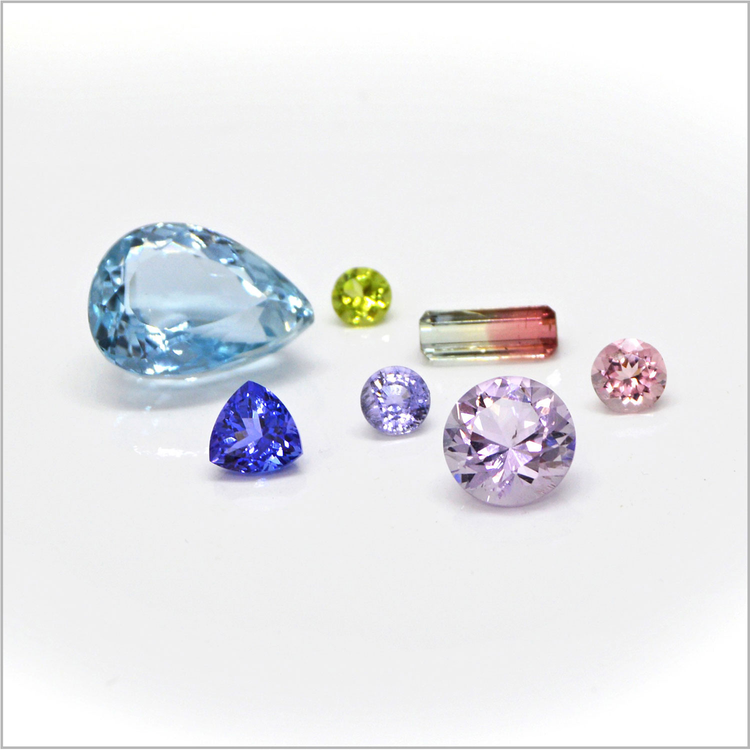 Assortment of colored faceted gemstones includinig pear-cut aquamarine, trillion-cut tanzanite, baguette bicolor tourmaline, and round rose quartz, pink and lavender sapphires and peridot