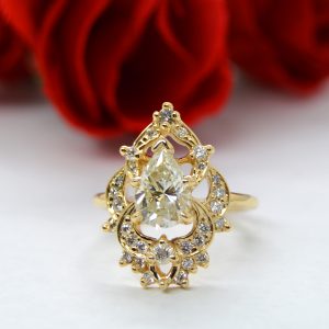 Custom engagement ring in 14K yellow gold with pear cut diamond, pave and prong set accents and open halo.